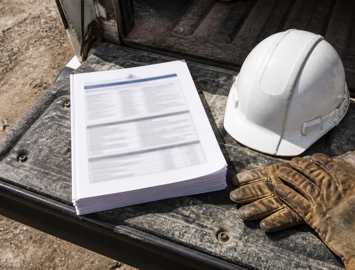 Printed site-specific safety plan on a pickup truck tailgate next to a hard hat and work gloves